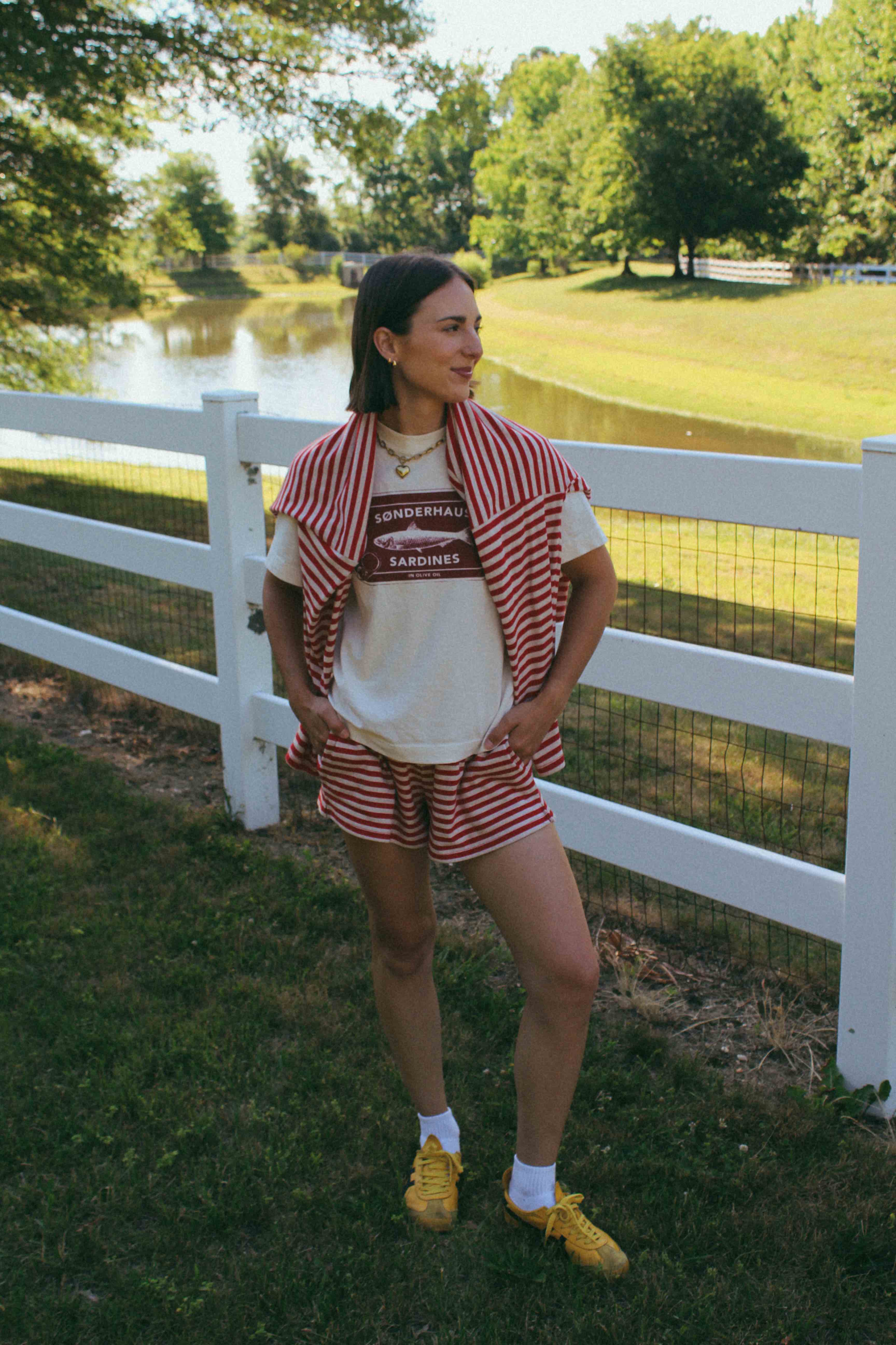 Person wearing a red and white striped shirt and shorts set with yellow sneakers, standing in a park.